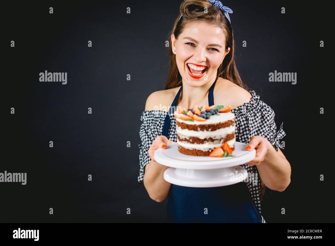 Vintage Frau mit verführerischen Lächeln hält einen hausgemachten Kuchen verlockend uns, es zu probieren Stockfoto