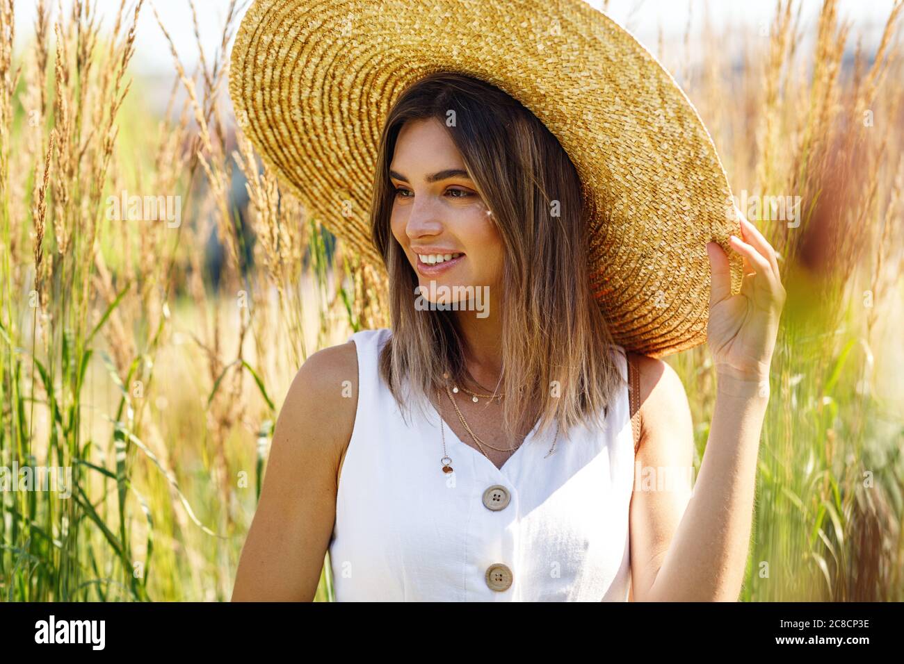 Porträt einer jungen lächelnden Frau, die einen großen Strohhut im Freien trägt Stockfoto