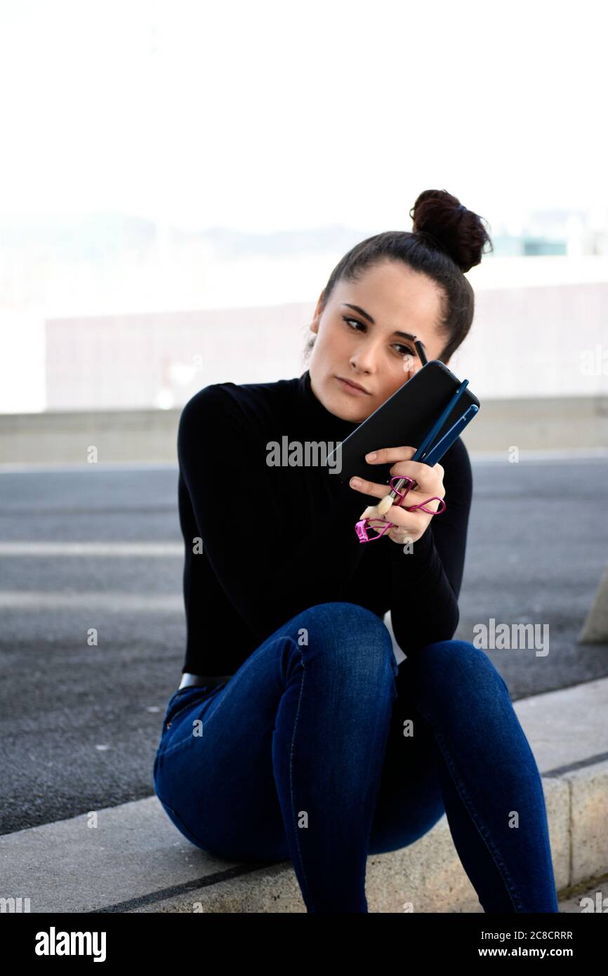 Vorderansicht eines jungen Mädchens mit Pferdeschwanz auf Treppen im Freien sitzen, während mit einem Make-up-Pinsel Stockfoto