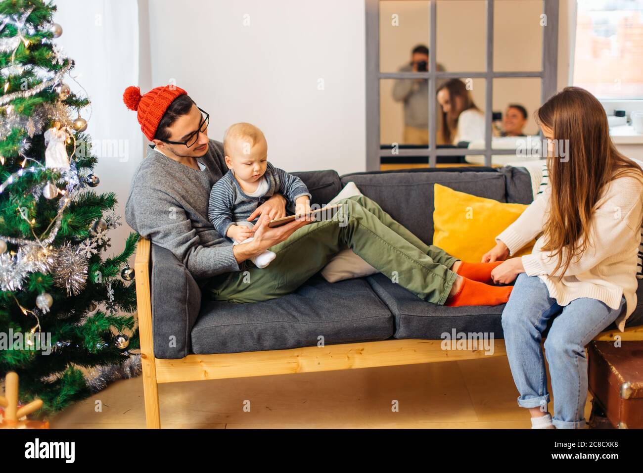 Baby mit Vater auf Sofa und mit digitalen Tablet während Weihnachten. Sohn und Eltern im Wohnzimmer während weihnachten. Stockfoto