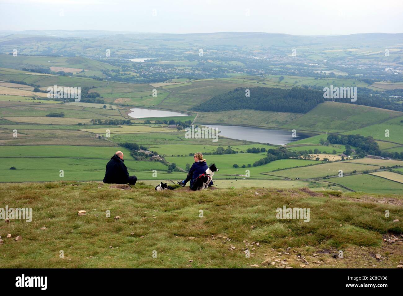 Ein Paar sitzt und genießt die Aussicht mit dort Hunde des schwarzen Moos Stauseen vom Gipfel des Pendle Hill, Gerste, Lancashire, Großbritannien. Stockfoto