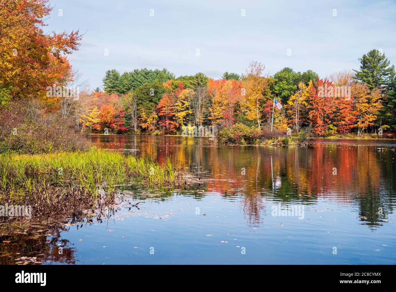 Fluss mit Banken in dichten Laubwald bedeckt. Atemberaubende Herbstfärbung. Eine kleine Insel mit US-Flagge ist in der Mitte des Flusses zu sehen. Stockfoto