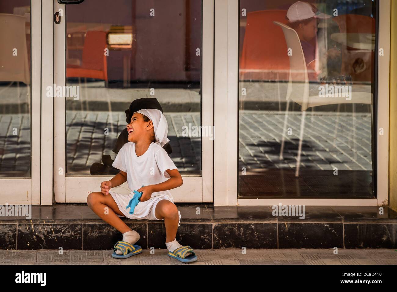 Havanna / Kuba - 04.15.2015: Süßes afro kubanisches Kind, das auf der Straße spielt, lacht und Spaß hat, während ein anderes Kind ein Telefonspiel drinnen spielt, sulki ist Stockfoto