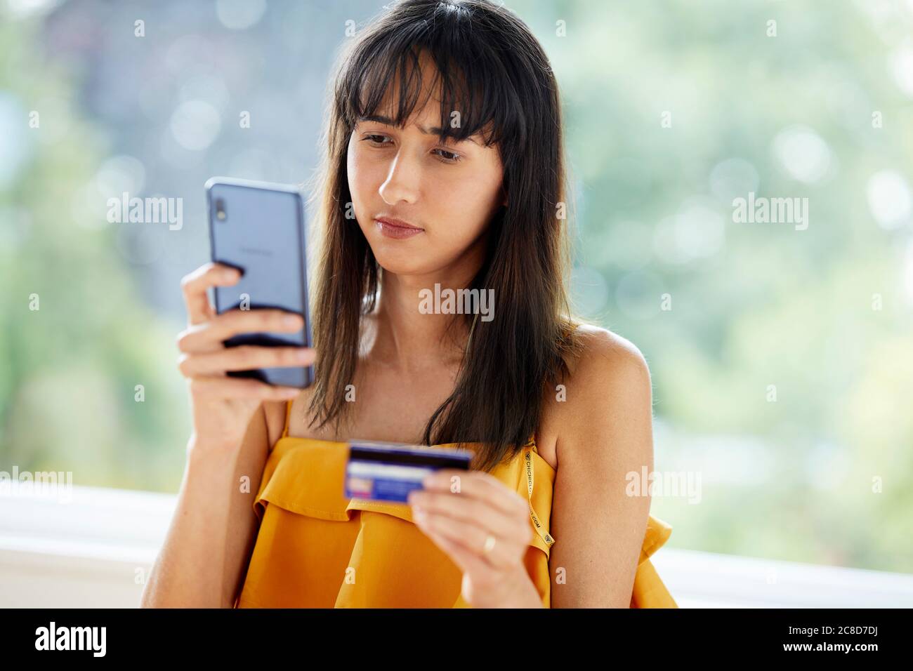 Frau, die auf ihr Telefon und ihre Kreditkarte schaut Stockfoto