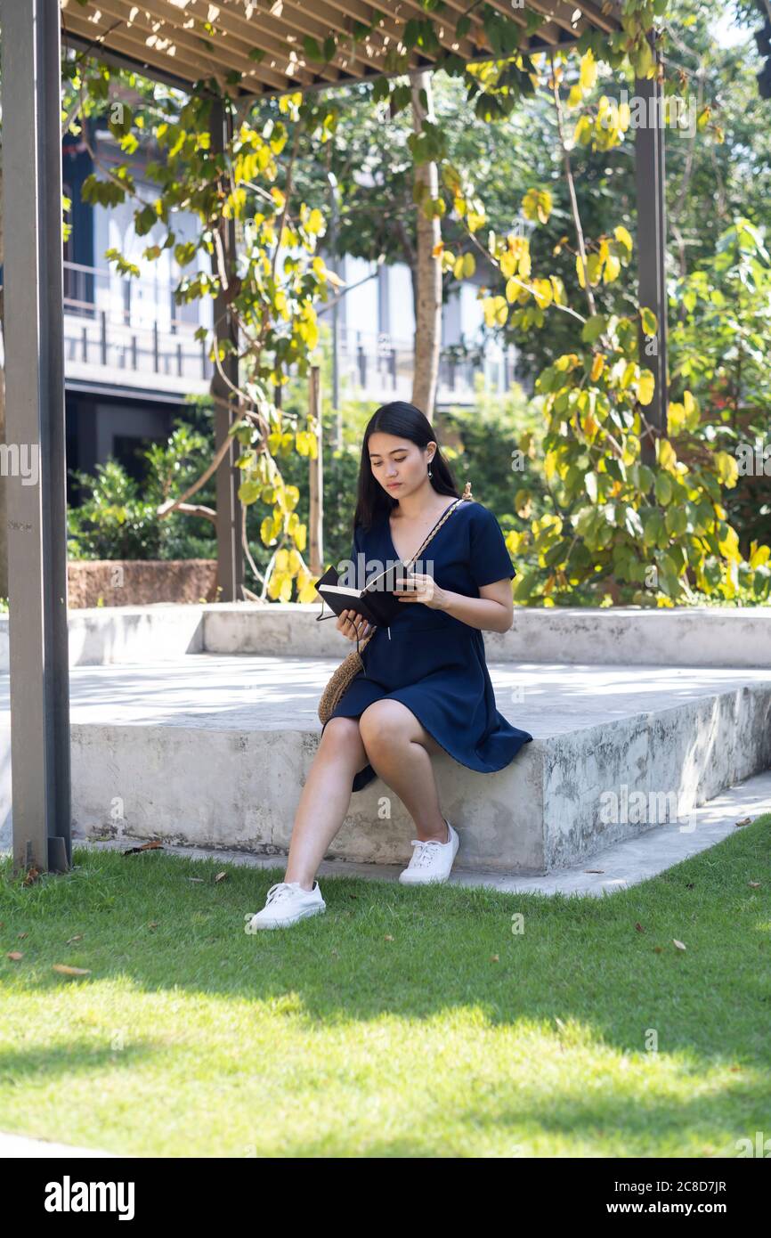 Lange Haare Frau auf der Steinbühne sitzen, das Buch lesen, während die Musik mit Kopfhörer hören, ihr Freund nicht rechtzeitig zu erscheinen. Stockfoto