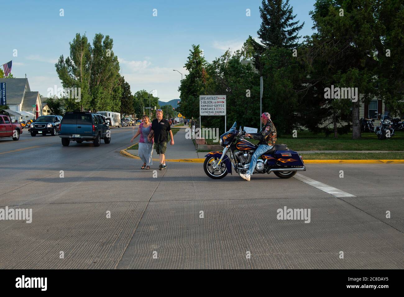 Sturgis, South Dakota - 9. August 2014: Straßenszene in der Stadt Sturgis mit einem Motorrad an einer Kreuzung geparkt und Fußgänger über die Stree Stockfoto