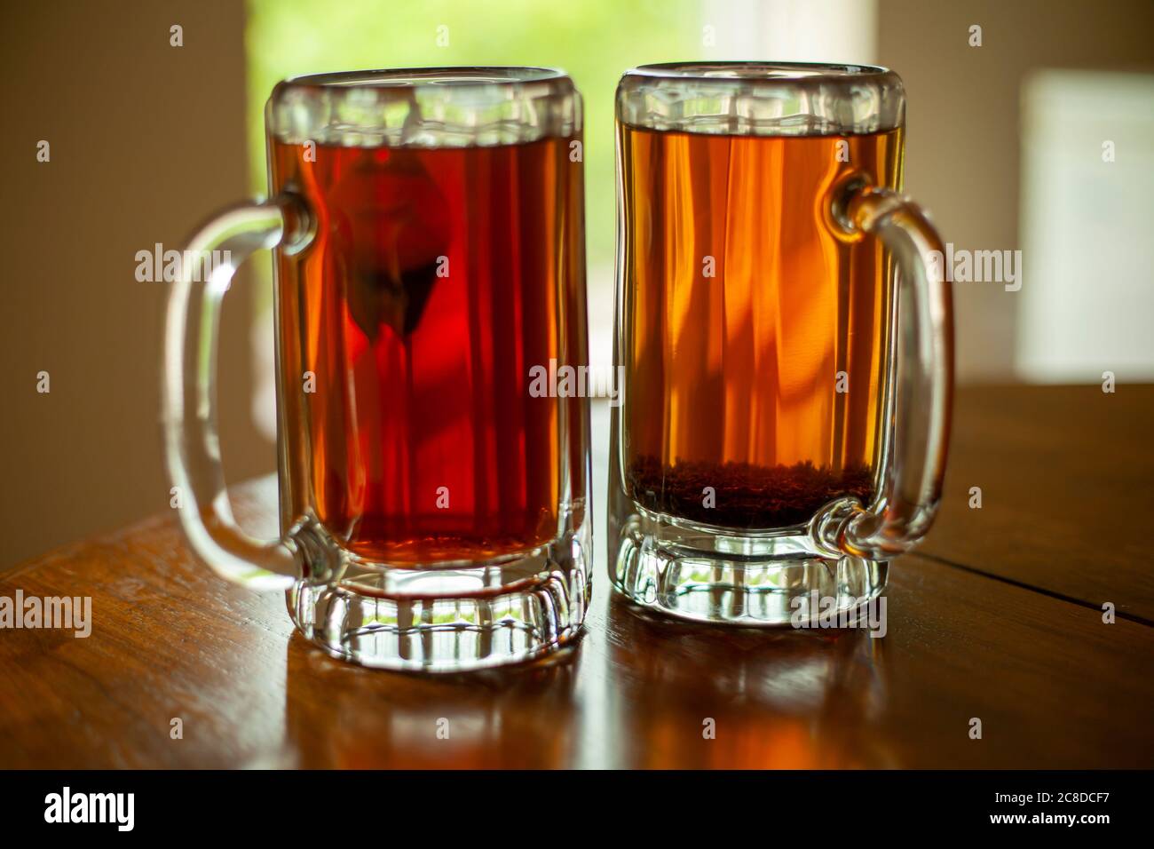 Nahaufnahme von zwei großen Glas Bierkrügen gefüllt mit frischem schwarzem Tee. Die Becher sitzen auf einer offenen Fensterbank mit Bäumen im Hintergrund. Stockfoto