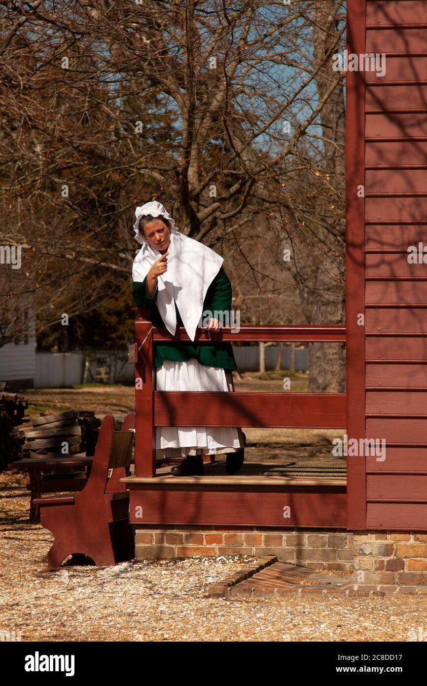 Williamsburg, Virgina, USA 02/22/2014: Porträt einer weißen Kolonialfrau, die am Geländer ihres historischen Bauernhauses steht und auf etwas zeigt. Stockfoto