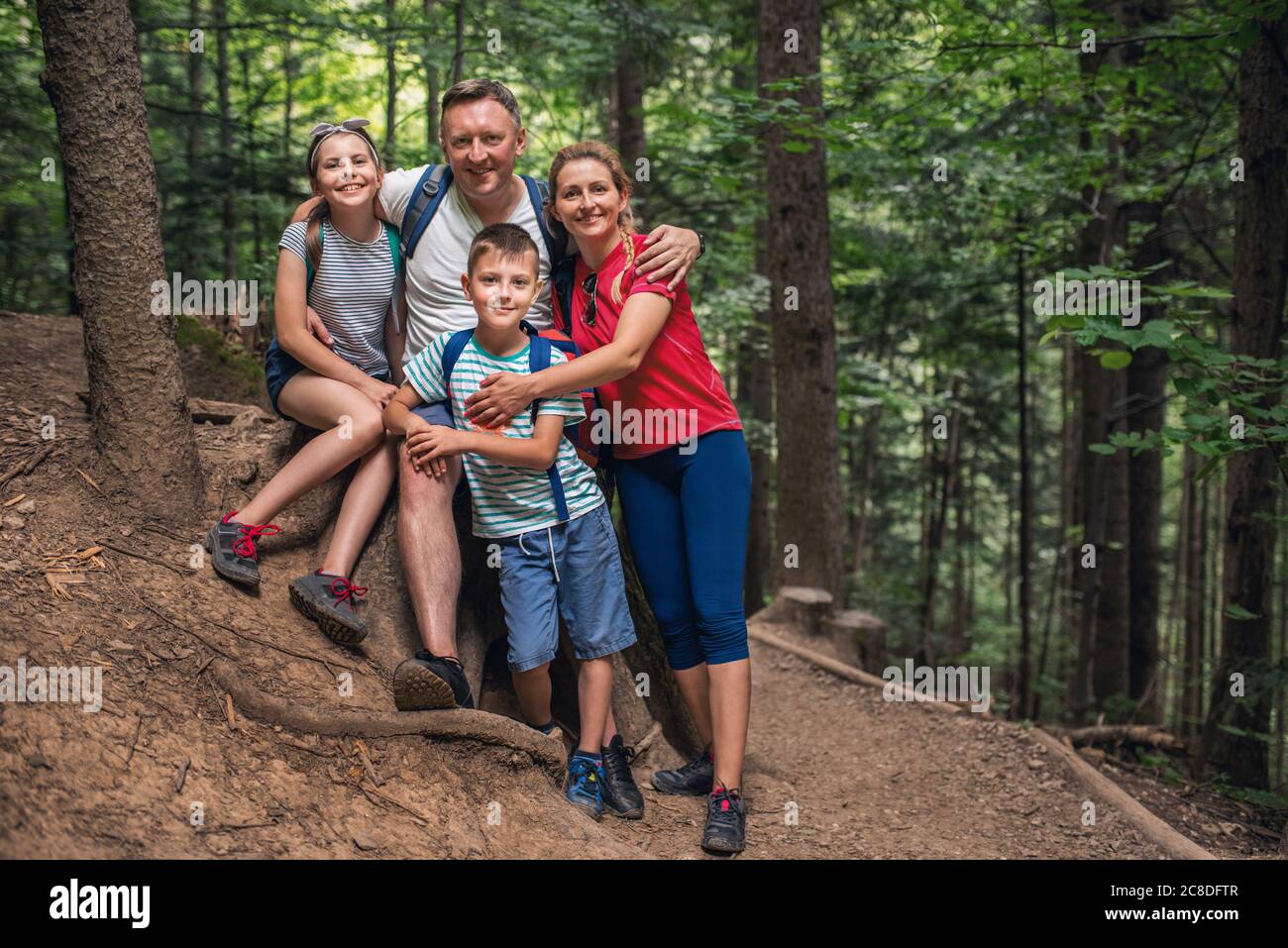 Portrait von lächelnden Eltern und ihren zwei kleinen Kindern, die auf einem Pfad in einem Wald zusammen stehen, während sie auf einer Wanderung sind Stockfoto