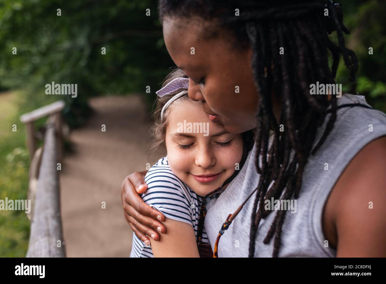 Lächelnde afroamerikanische Frau umarmte liebevoll ein kleines Mädchen, während sie eine Pause von ihrer Wanderung zusammen Stockfoto