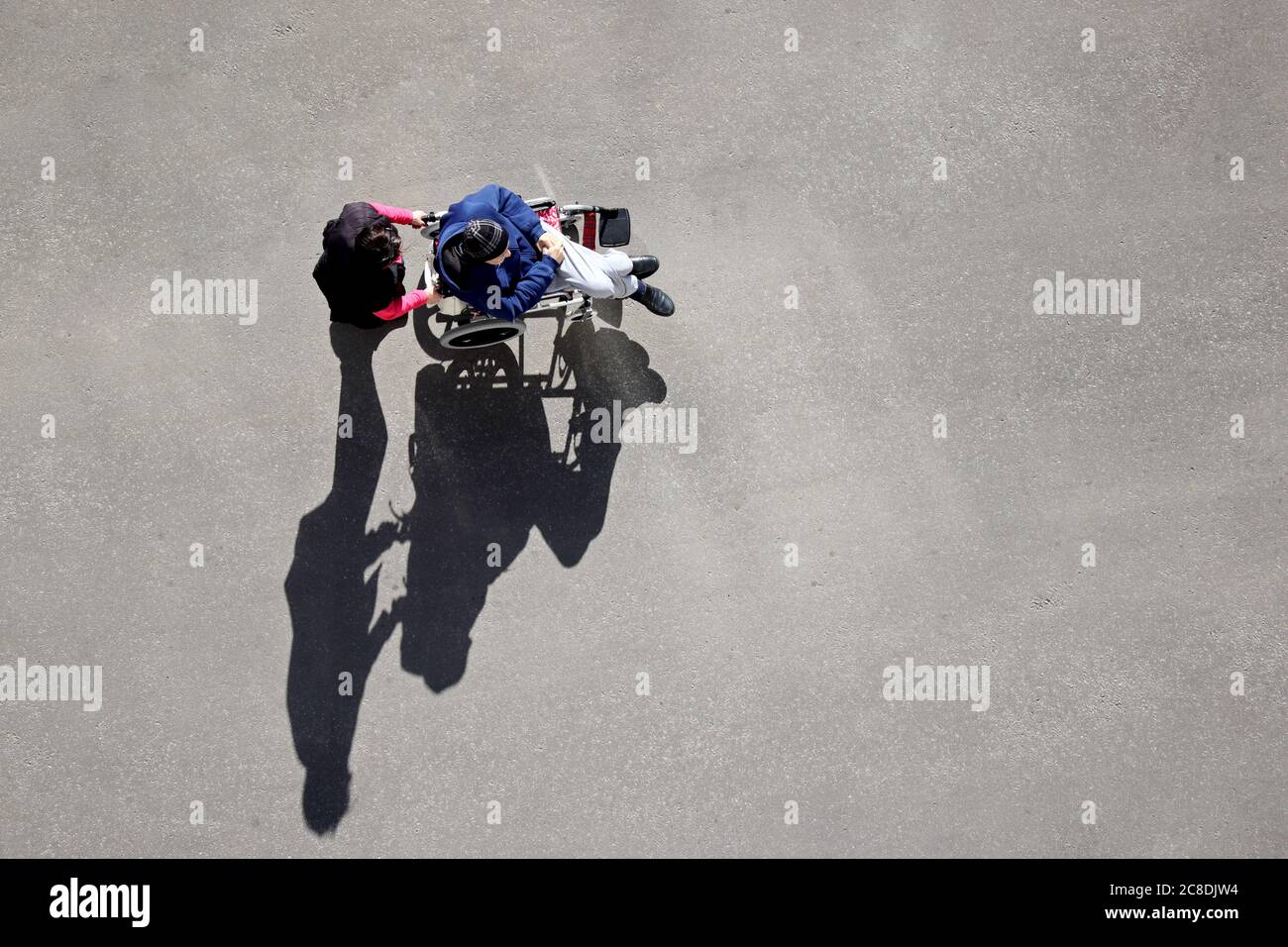 Frau trägt eine behinderte Person im Rollstuhl auf einer Straße der Stadt, Draufsicht. Krankenschwester und älterer Mann, Betreuung für behinderte Menschen Stockfoto