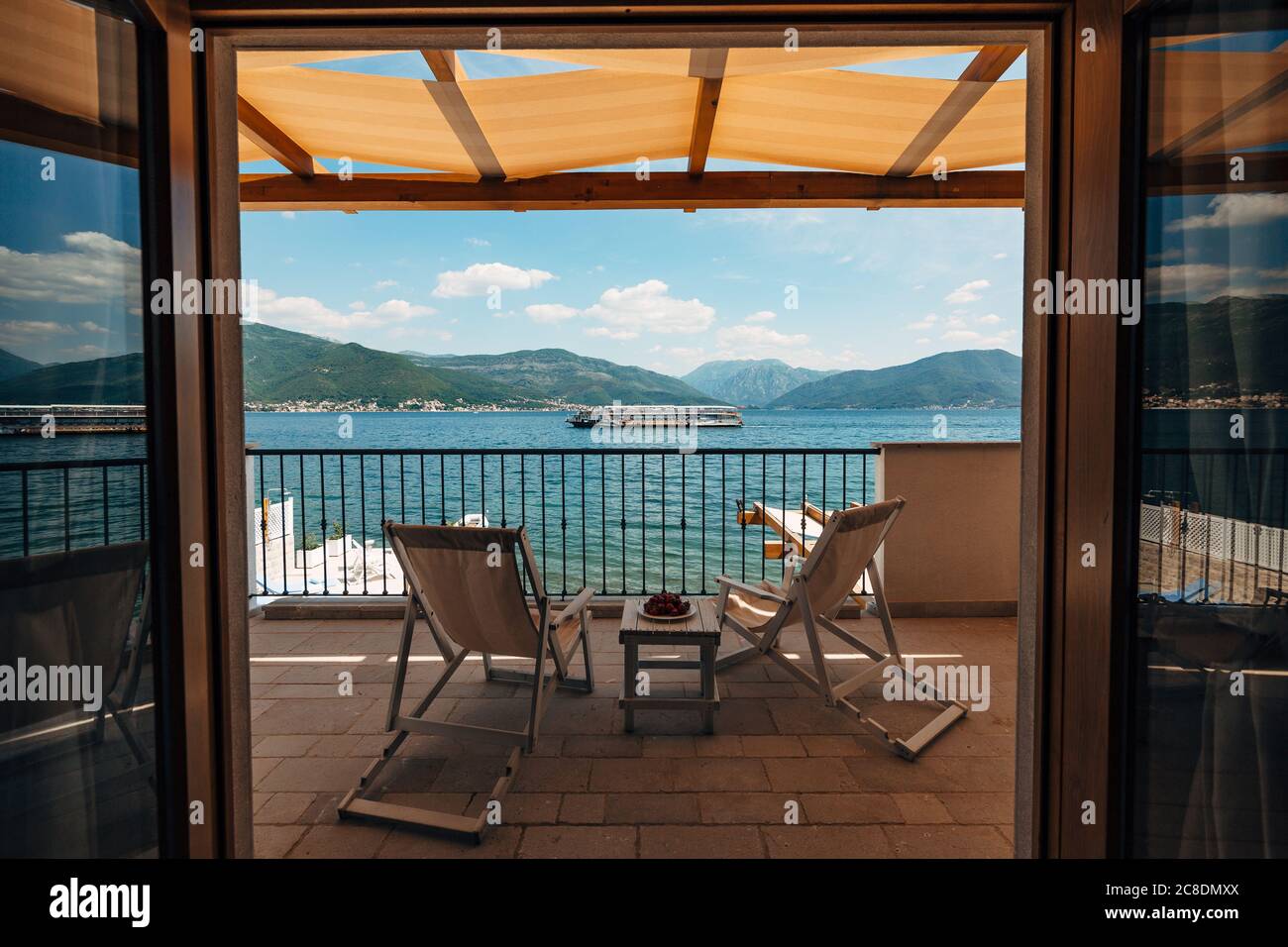 Zwei Sonnenliegen auf dem Balkon des Hotelzimmers mit Blick auf das Meer und ein vorbeifahrenden Touristenboot. Stockfoto