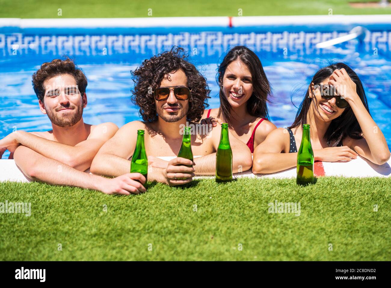 Lächelnde junge multiethnische Freunde mit Bierflaschen genießen den Sommer in Swimmingpool im Hinterhof Stockfoto