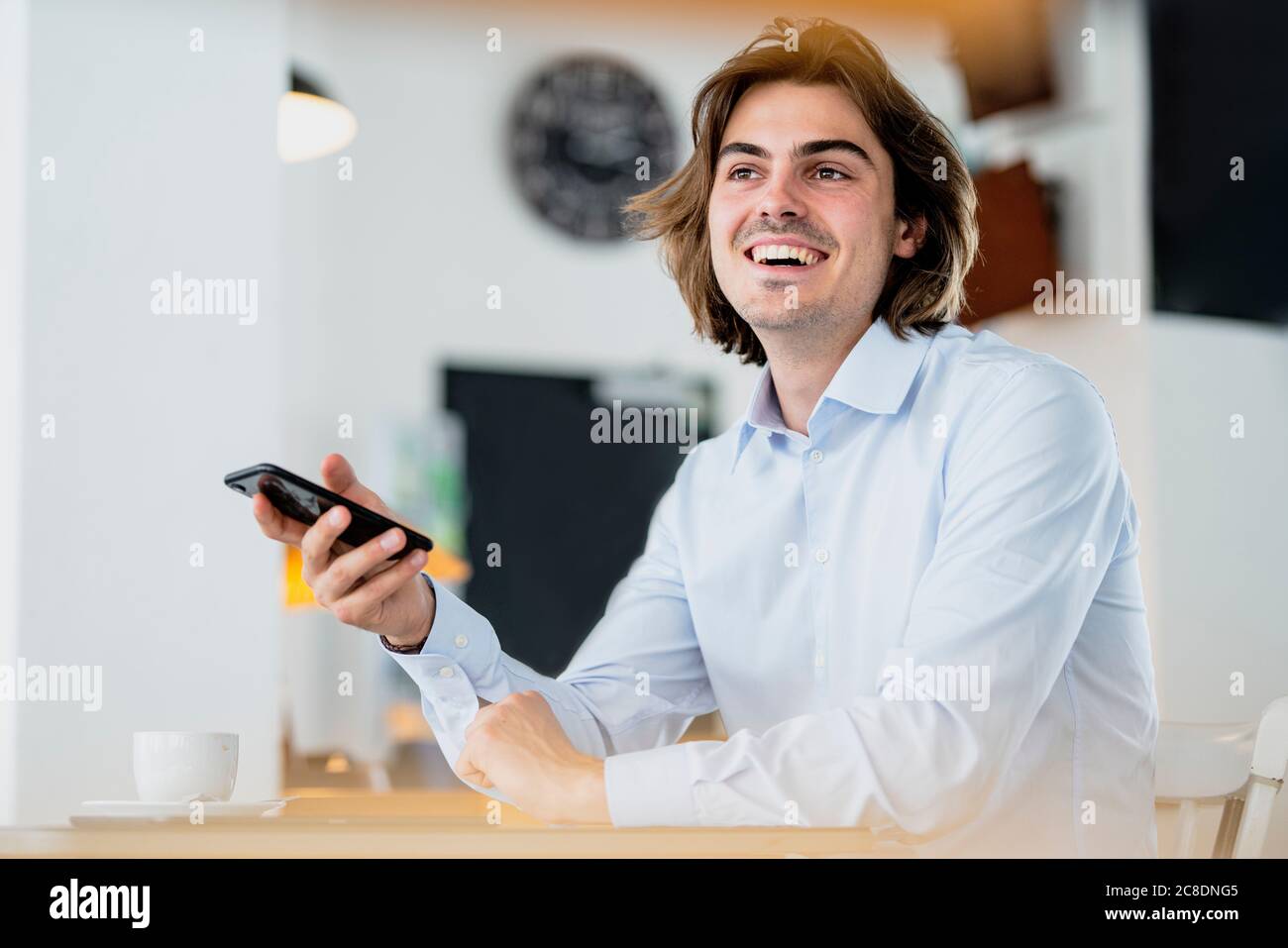Fröhlicher Geschäftsmann hält Smartphone, während er im Café sitzt Stockfoto