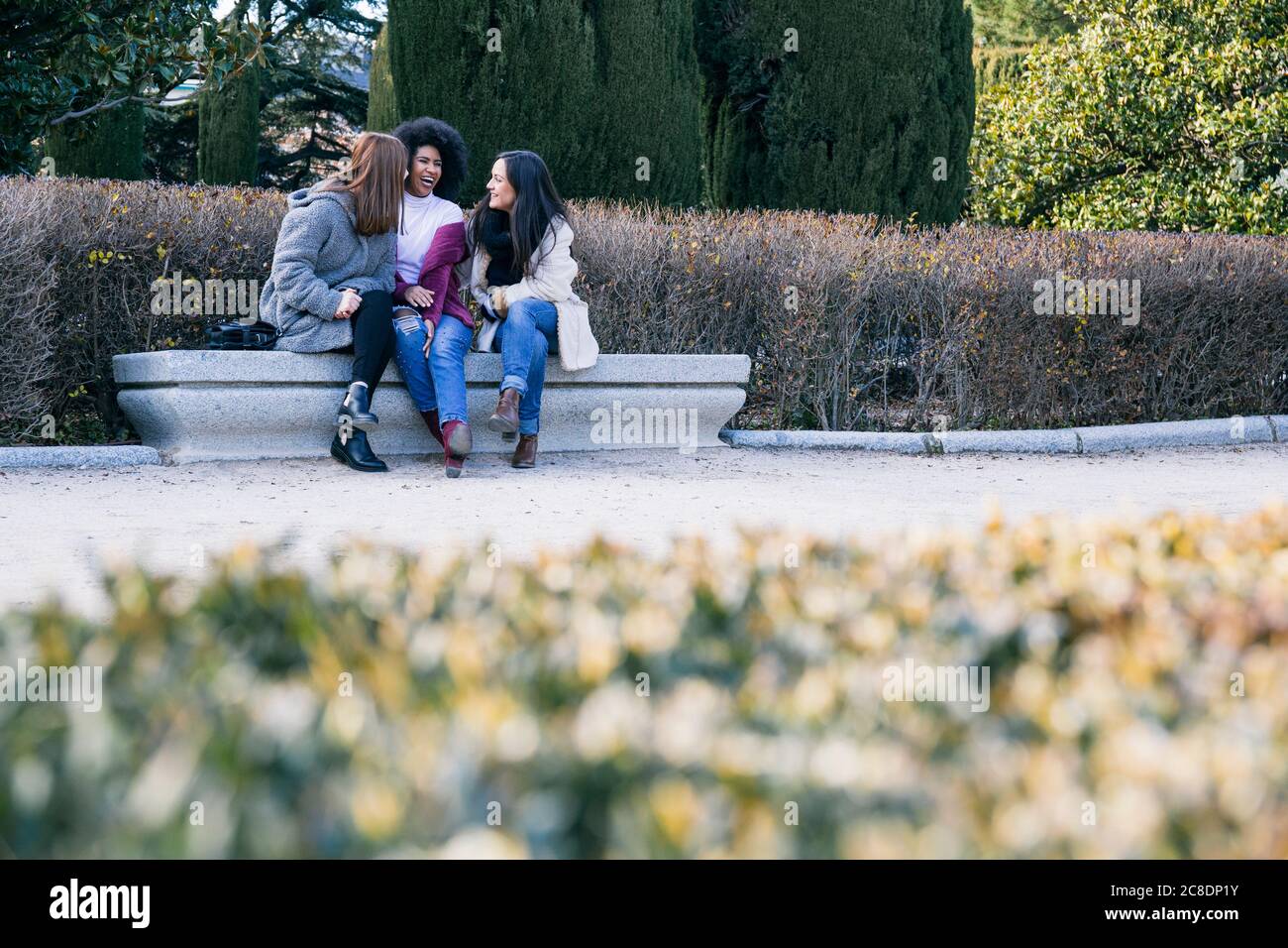 Glückliche multiethnische Freundinnen, die auf der Parkbank sitzen und sich unterhalten Stockfoto