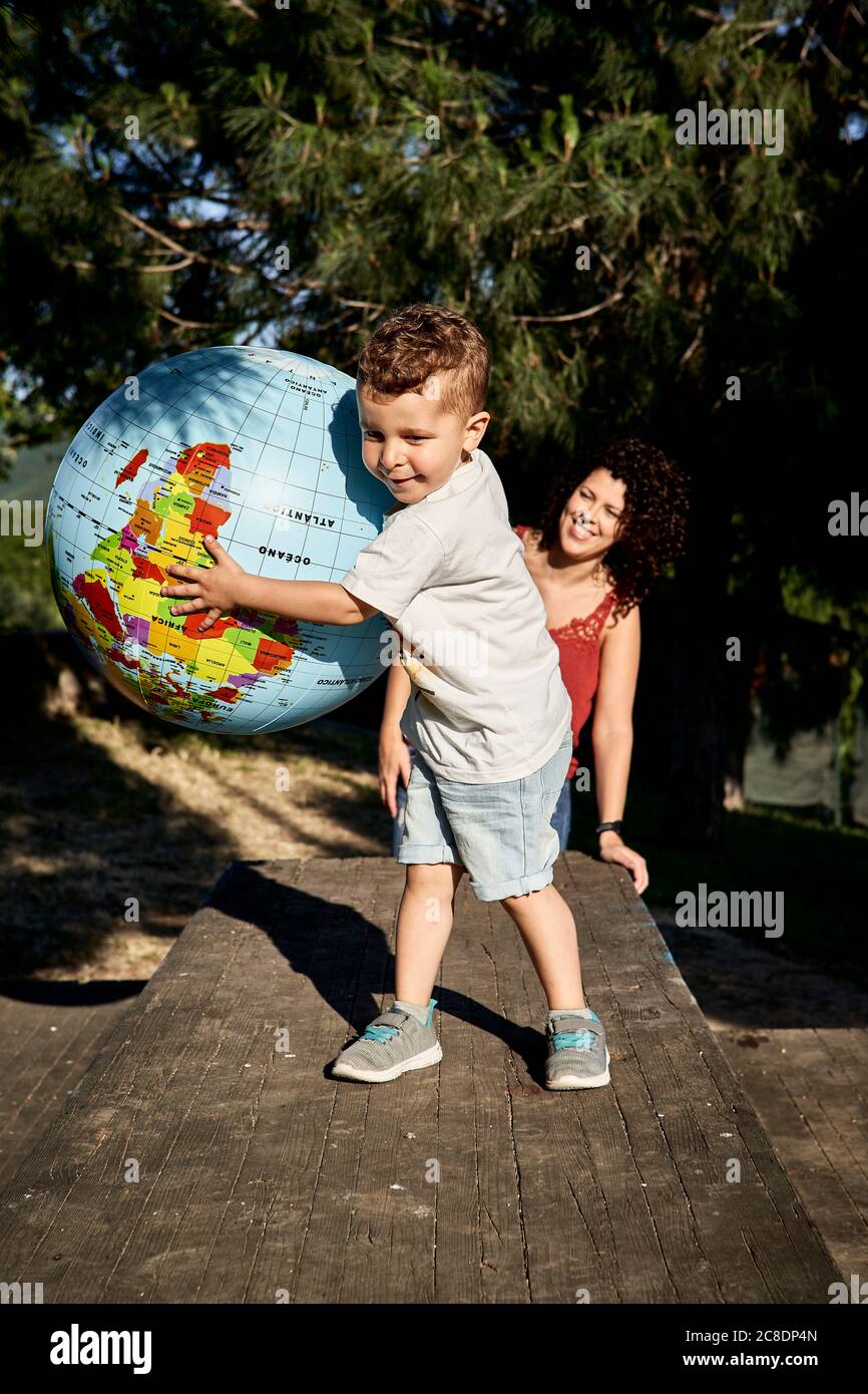 Lächelnde Mutter, die den Sohn anschaut, der mit Globus auf dem Tisch spielt Stockfoto