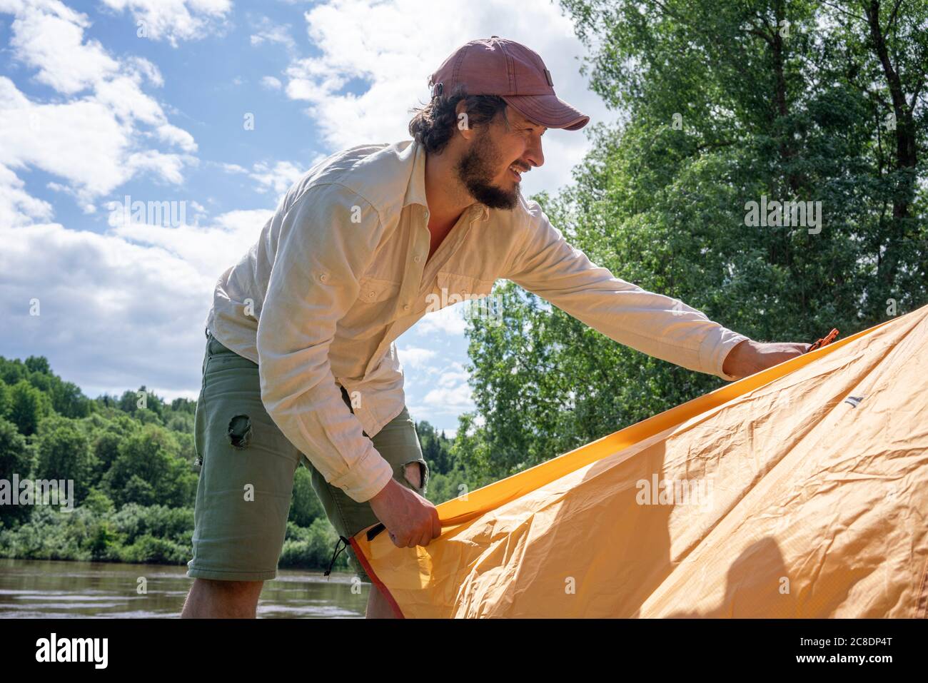 Mittelerwachsener Mann, der Zelt im Wald gegen den Himmel installiert Campingplatz Stockfoto