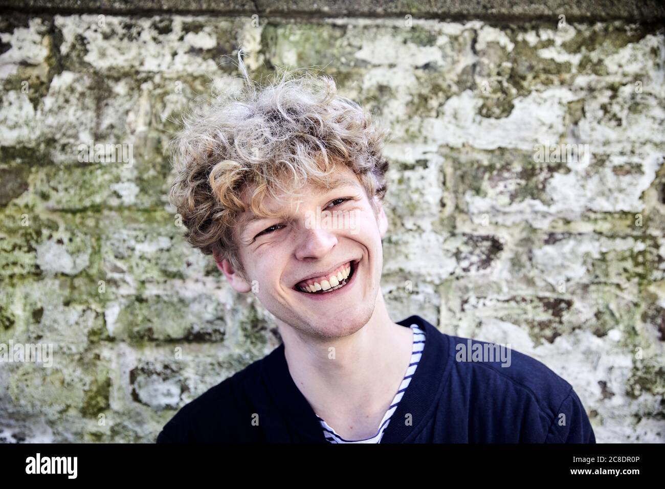 Porträt des lachenden jungen Mannes mit lockigen blonden Haaren in Vorderseite der verwitterten Wand Stockfoto