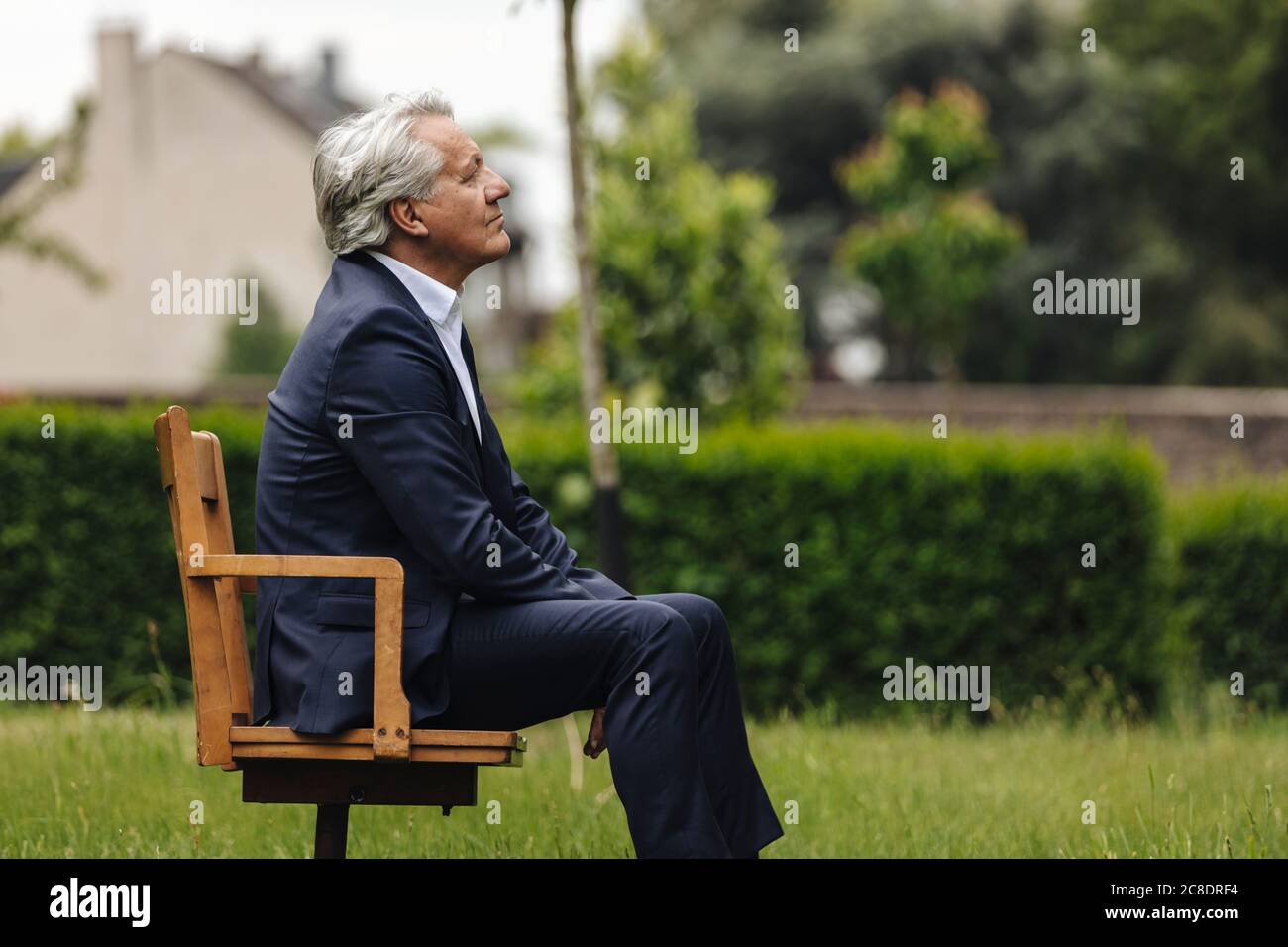 Ein älterer Geschäftsmann sitzt auf einem Stuhl in einem ländlichen Garten Stockfoto