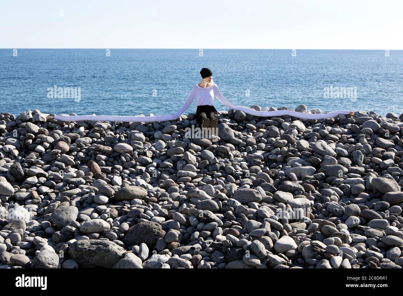 Frau mit künstlichen langen Händen sitzt auf Kieselsteinen am Strand An sonnigen Tagen Stockfoto