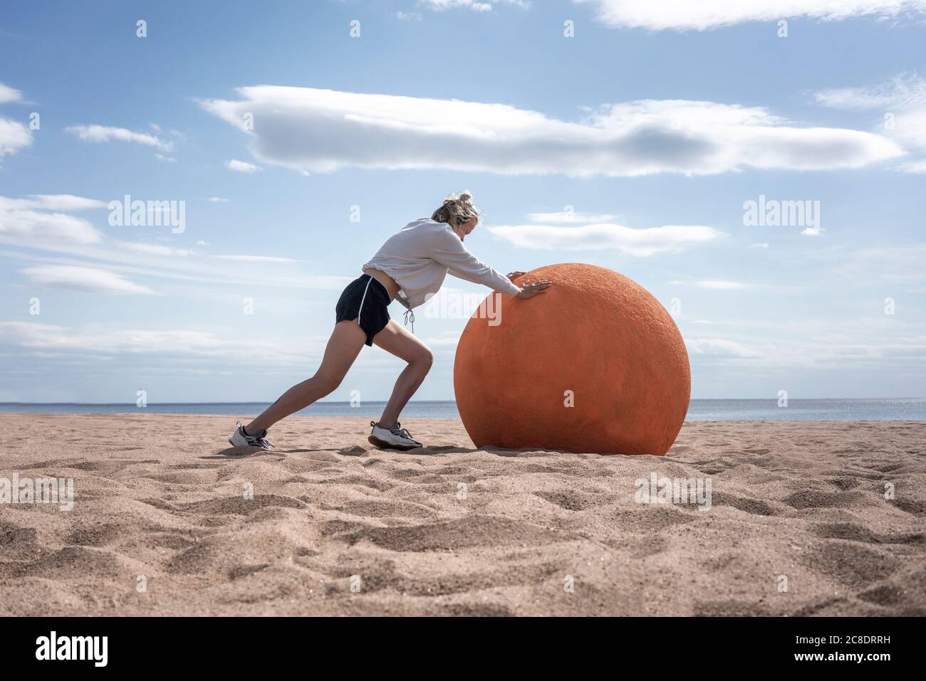 Junge Frau rollt Orangenstein am Strand Stockfoto