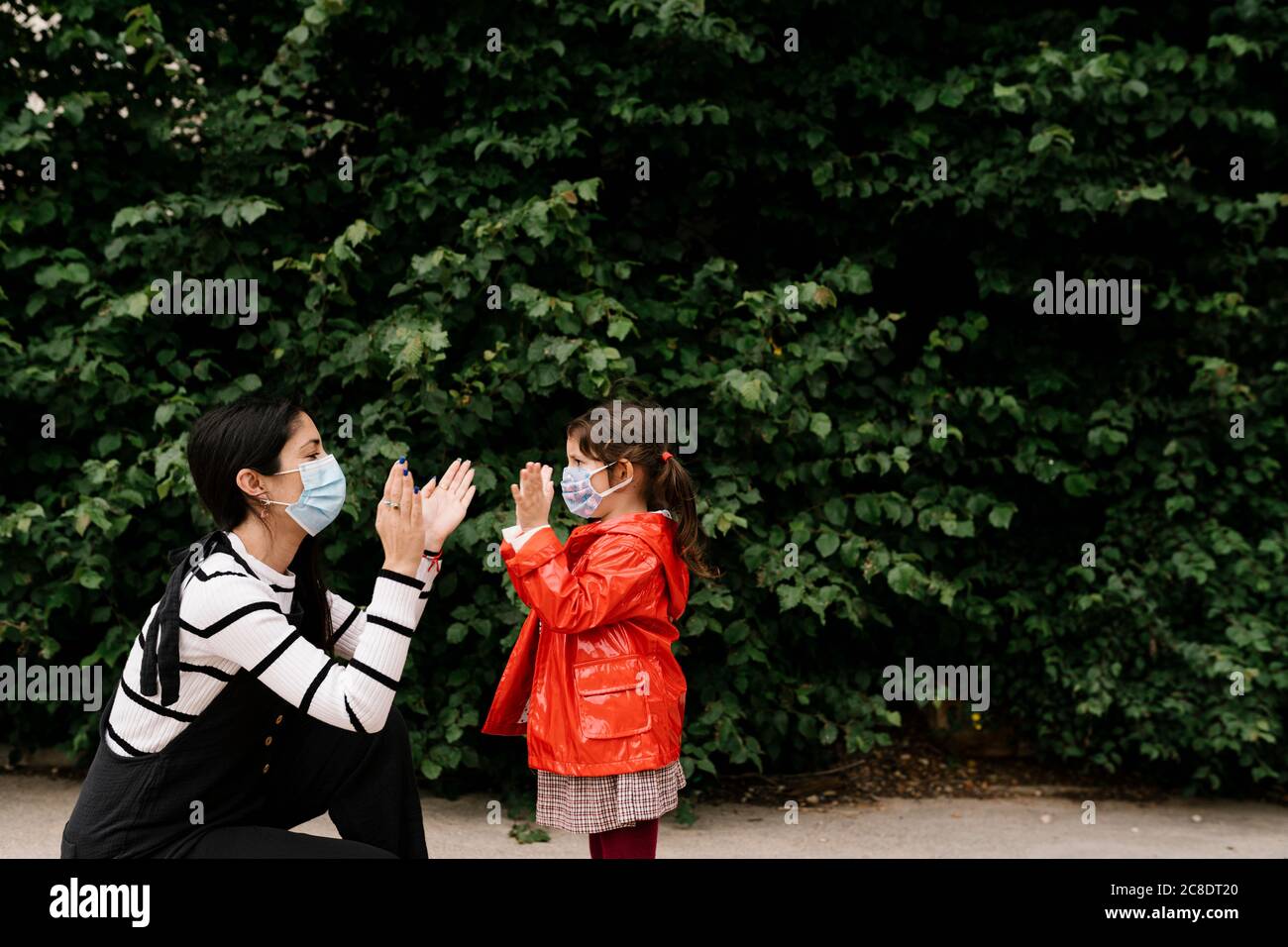 Mutter und Tochter tragen Masken beim Klatschen Spiel gegen Anlagen Stockfoto