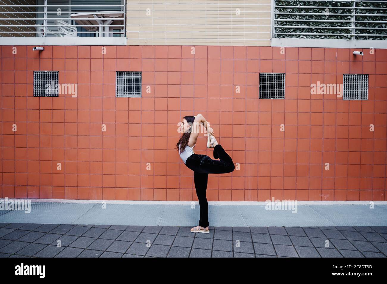 Junge Frau, die Yoga auf dem Bürgersteig gegen geflieste Wand in Stadt Stockfoto