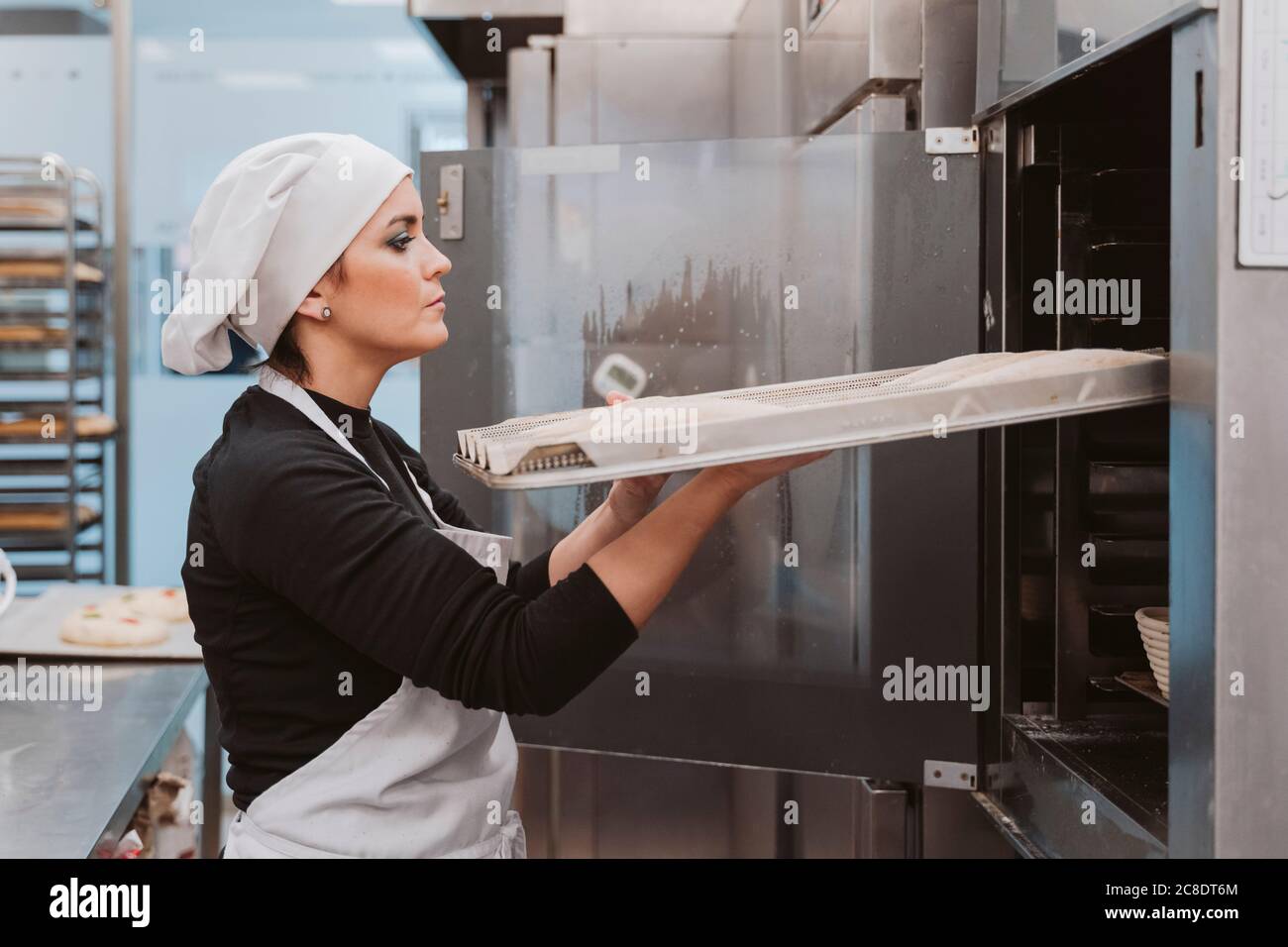 Weibliche Bäcker Einlegen Backblech im Ofen bei der Bäckerei Stockfoto