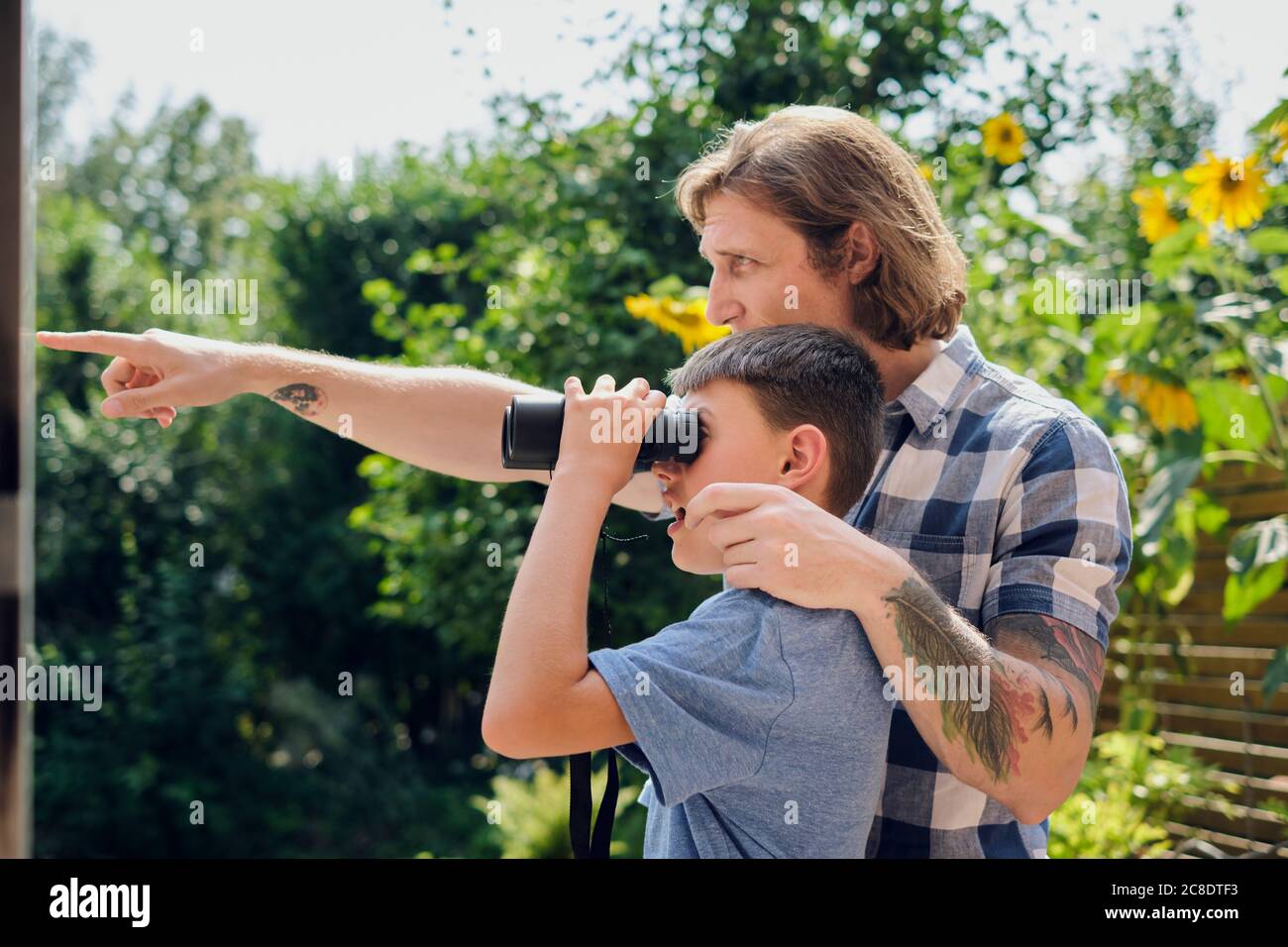 Vater zeigt dem Sohn etwas, der durch ein Fernglas auf den Hof schaut An sonnigen Tagen Stockfoto