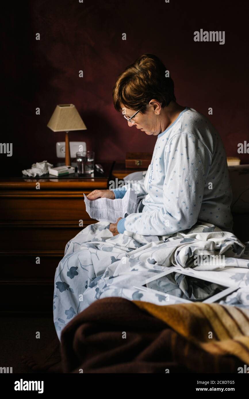 Ältere Frau im Ruhestand liest Anweisungen von verschreibungspflichtigen Medikamenten während des Sitzens Auf dem Bett zu Hause Stockfoto