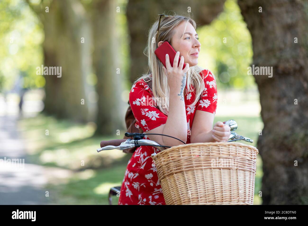 Nachdenkliche Frau, die Smartphone benutzt, während sie sich auf dem Fahrrad anlehnt Öffentlicher Park Stockfoto