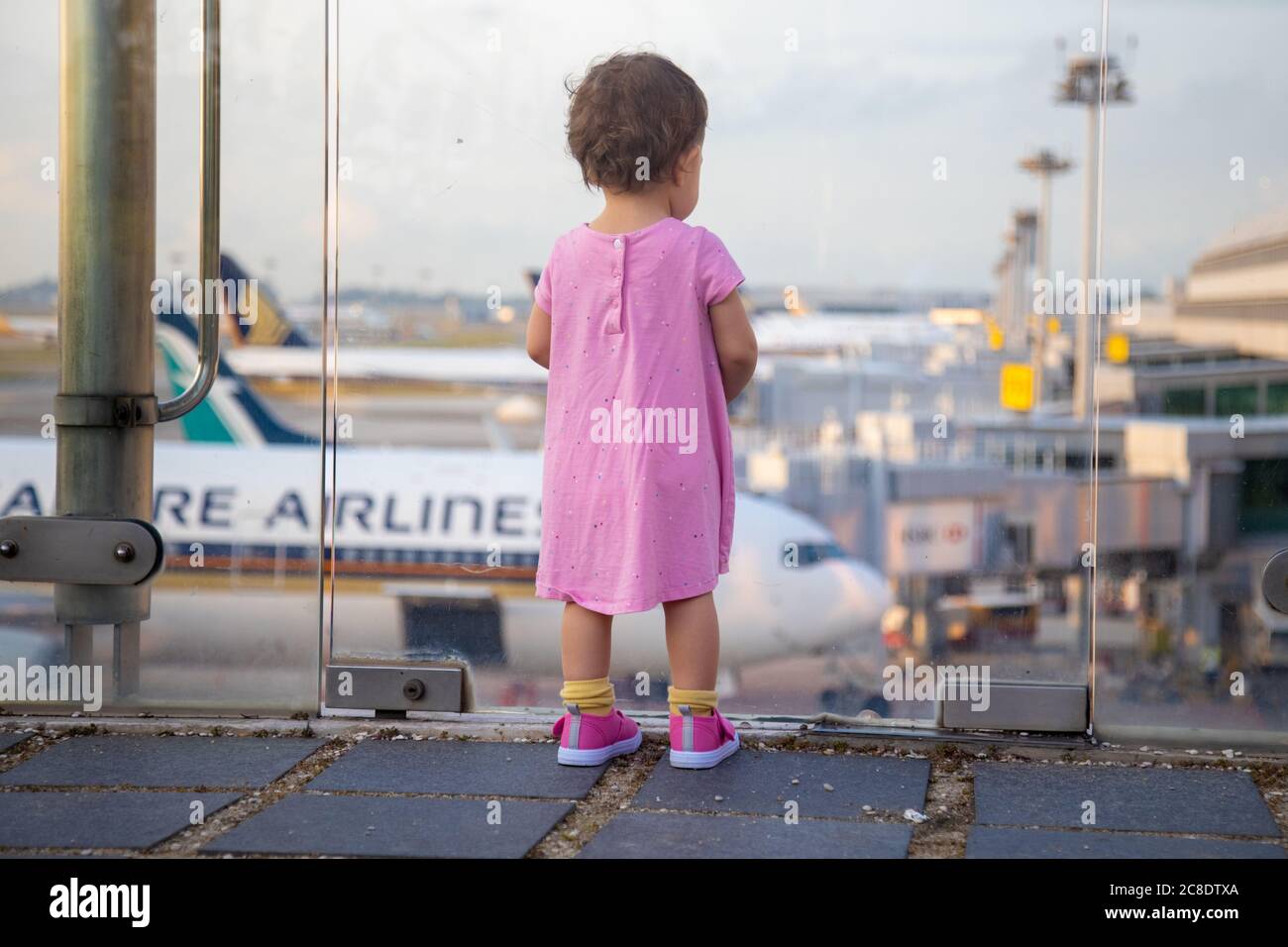 SINGAPUR - FEBRUAR 11 2020: Kleinkind in Pink Dress sieht sich Singapore Airlines geparkte Flugzeuge am Changi Airport an Stockfoto