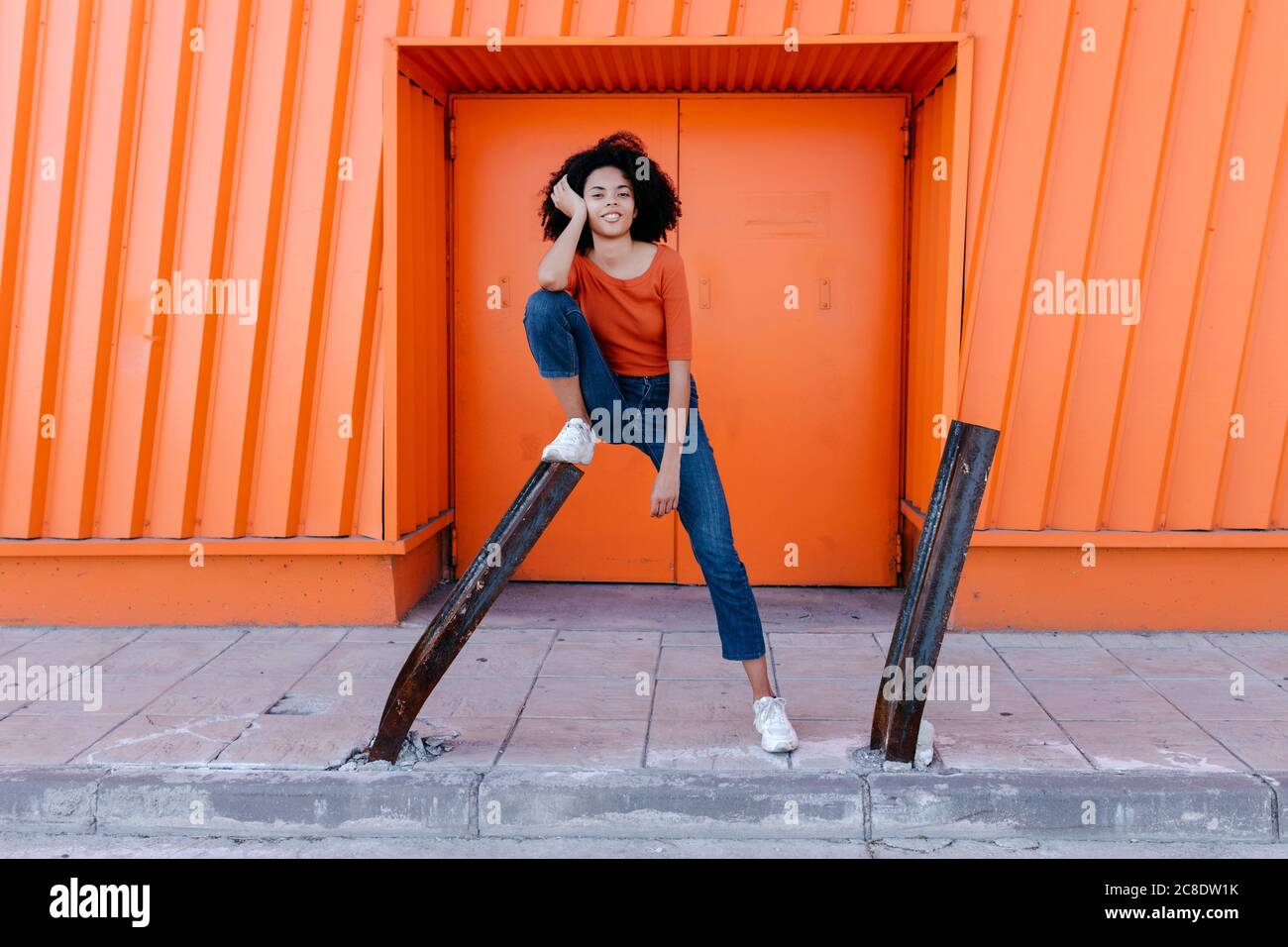 Lächelnd junge afro Frau lehnte sich auf Metall mit der Hand in Haare gegen orangefarbene Tür Stockfoto