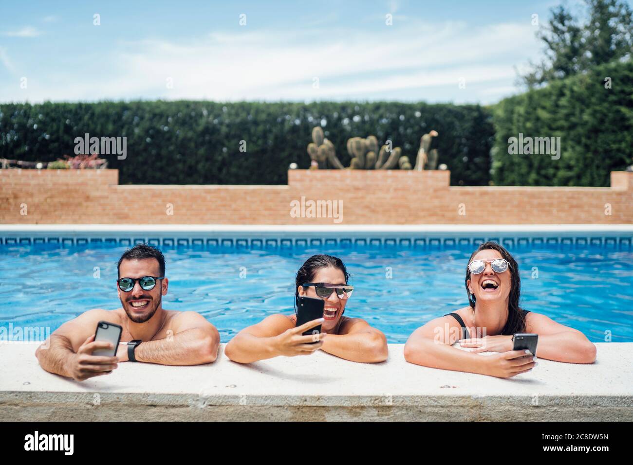 Lachende Freunde während der Poolparty mit Smartphones Stockfoto