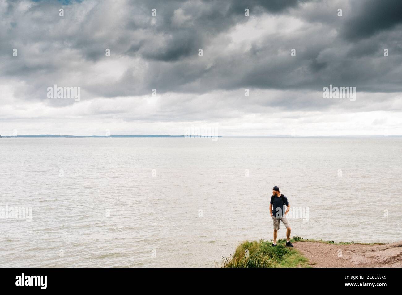 Mann, der auf einer Klippe steht, während er gegen Sturm auf das Meer blickt Wolken Stockfoto