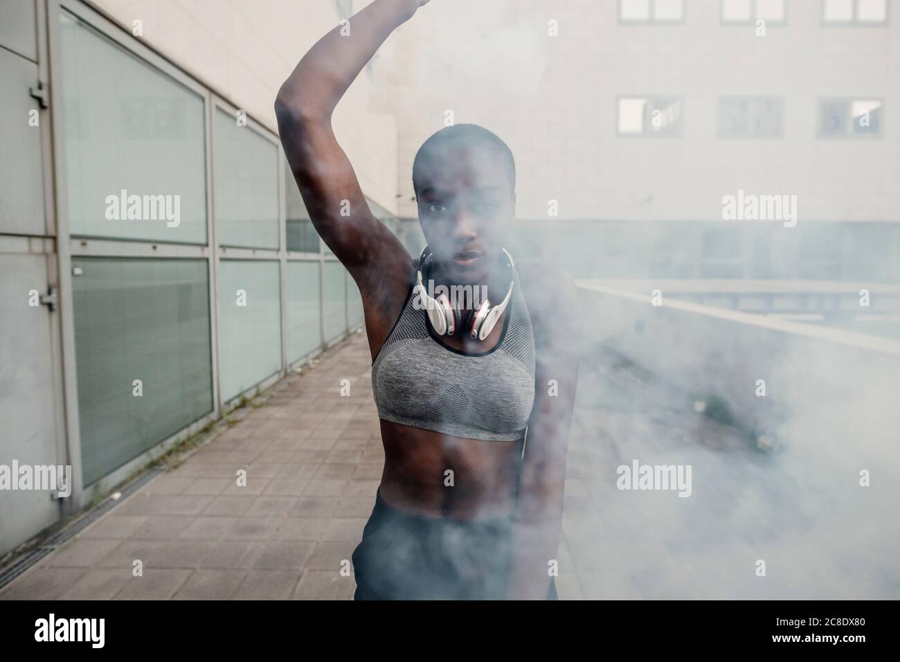 Junge Frau spielt mit Rauchbombe, während sie gegen Gebäude steht In der Stadt Stockfoto