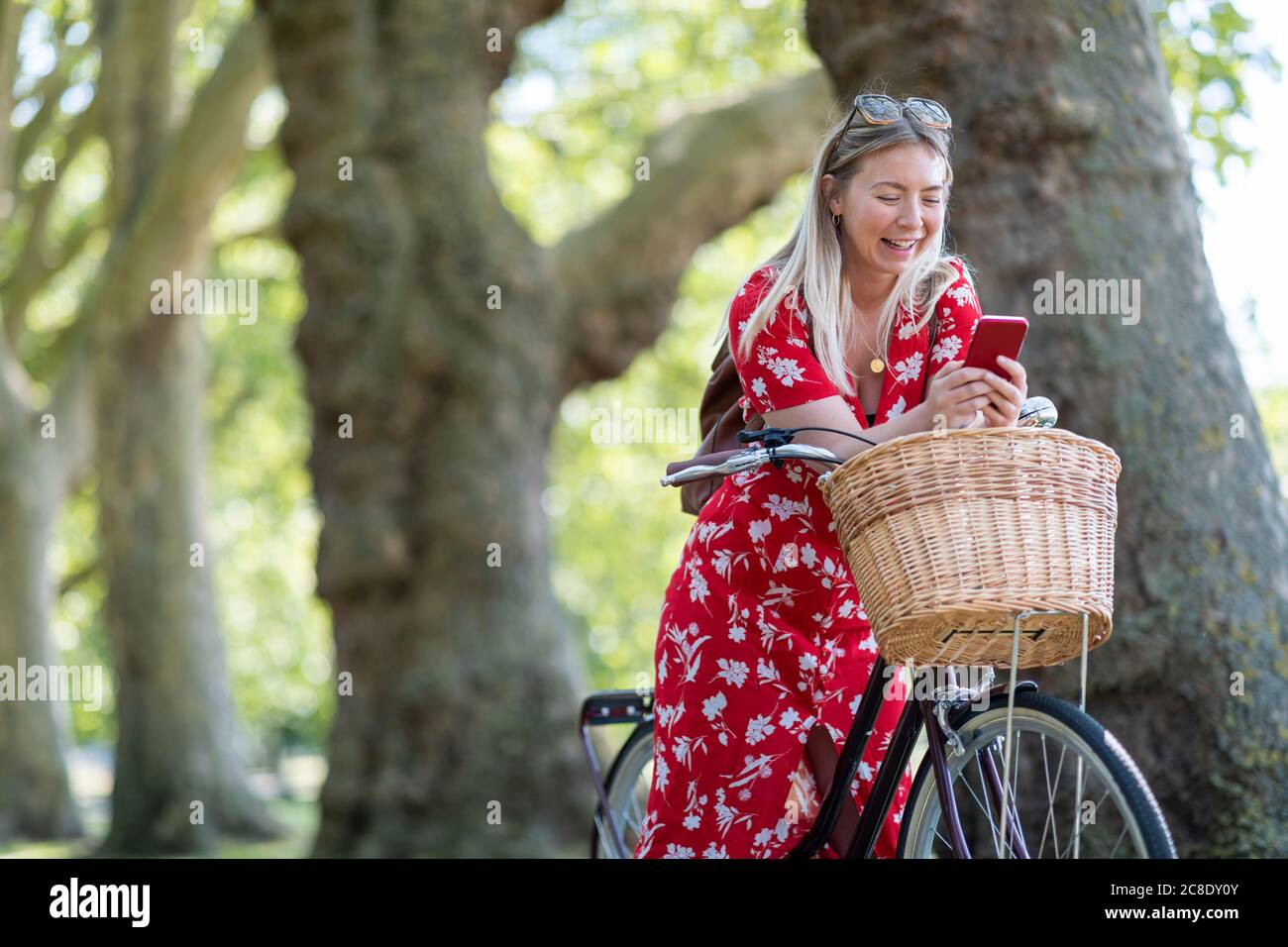 Fröhliche Frau mit Smartphone, während sich auf Fahrrad an Öffentlicher Park Stockfoto