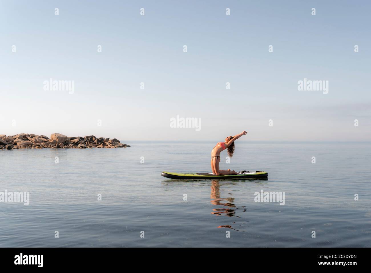 Reife Frau, die Yoga auf dem Paddleboard auf dem Meer gegen den Himmel praktiziert Stockfoto