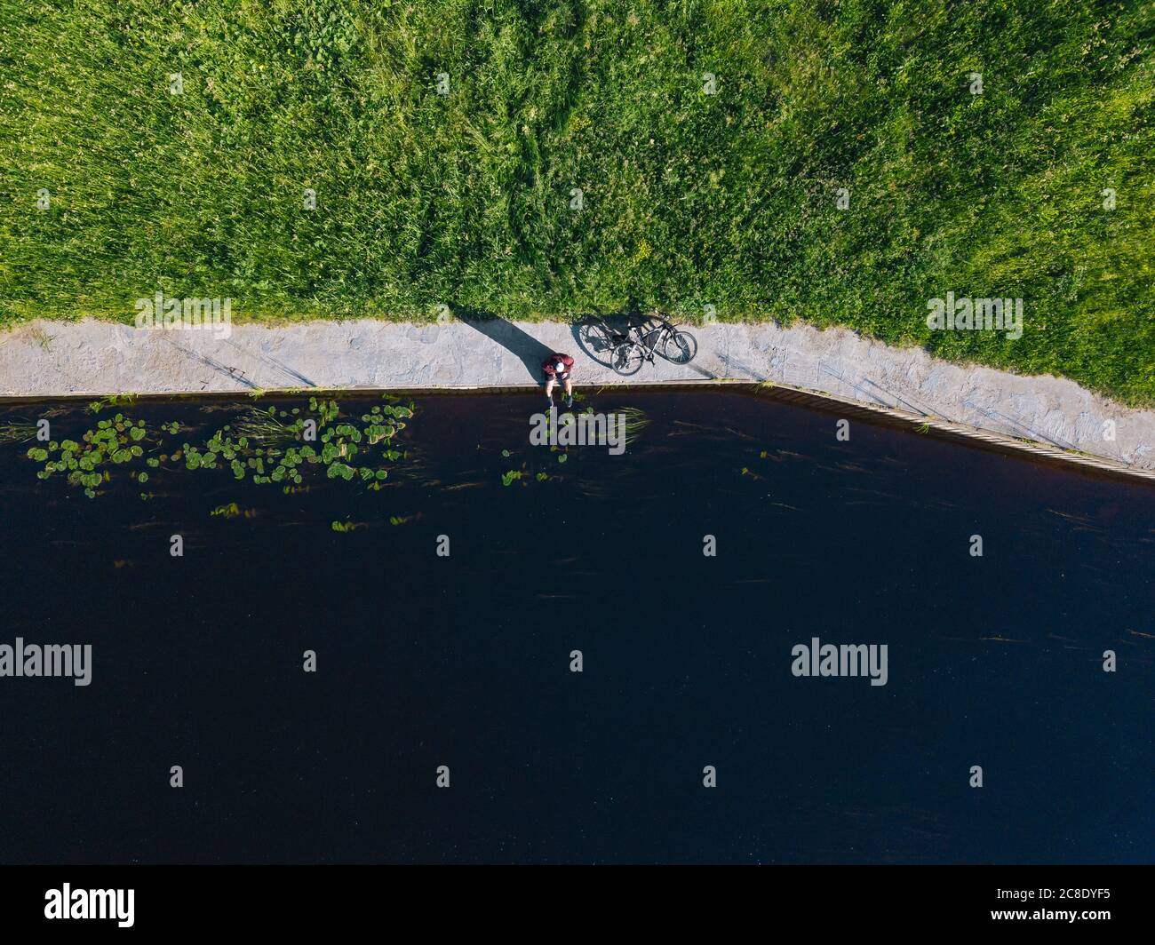 Drohnenaufnahme eines mittelerwachsenen Mannes mit einem Fahrrad, an dem er sitzt Flussküste Stockfoto