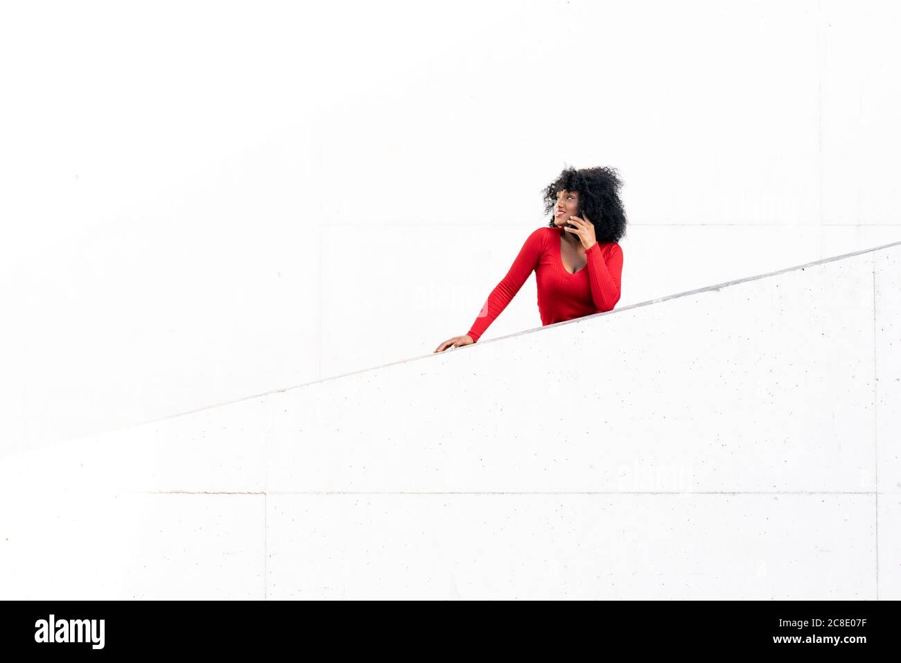 Junge Frau mit afro Haar mit Smartphone auf weiße Rampe Stockfoto