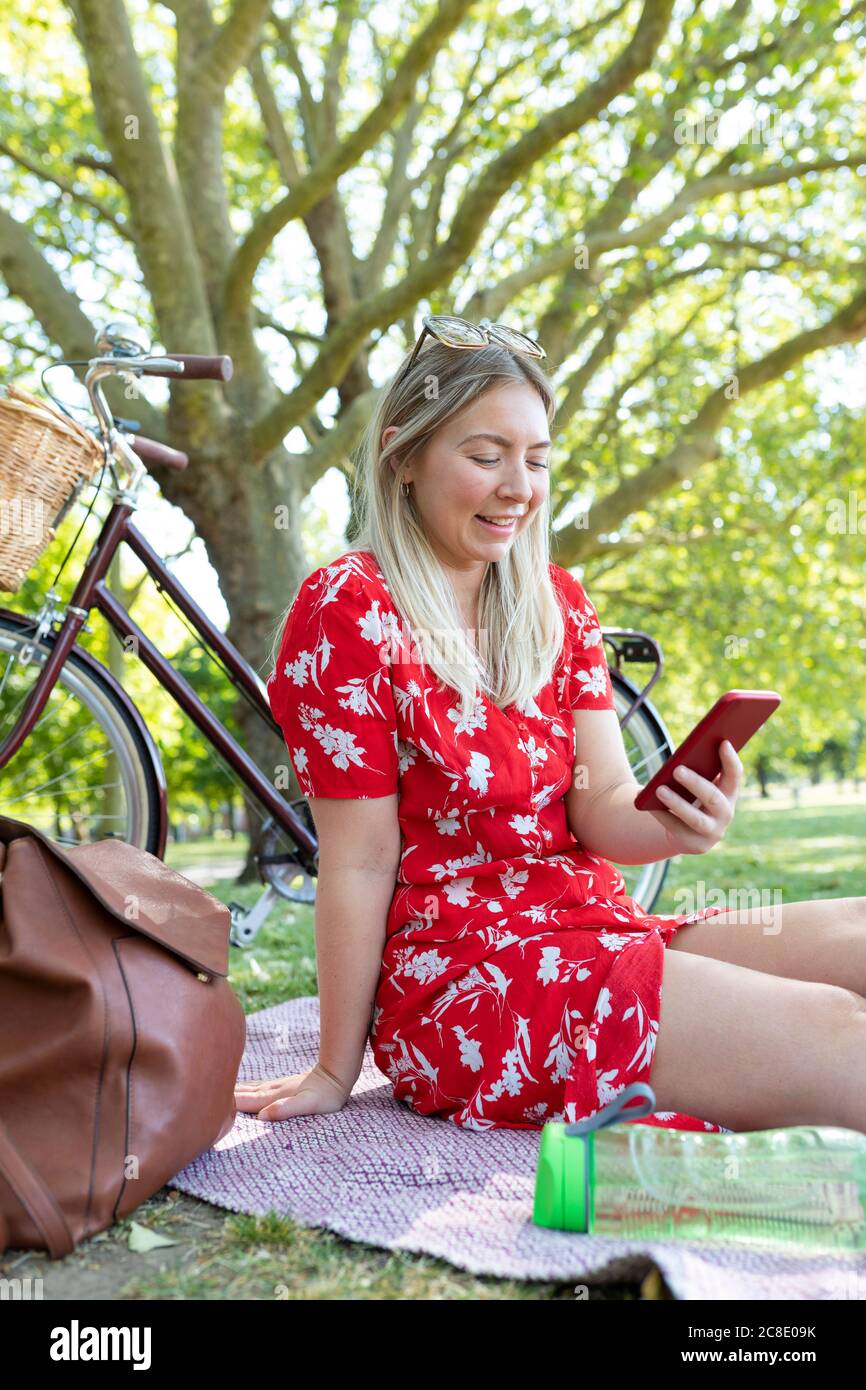 Glückliche Frau mit Smartphone, während sie im öffentlichen Park sitzt Stockfoto