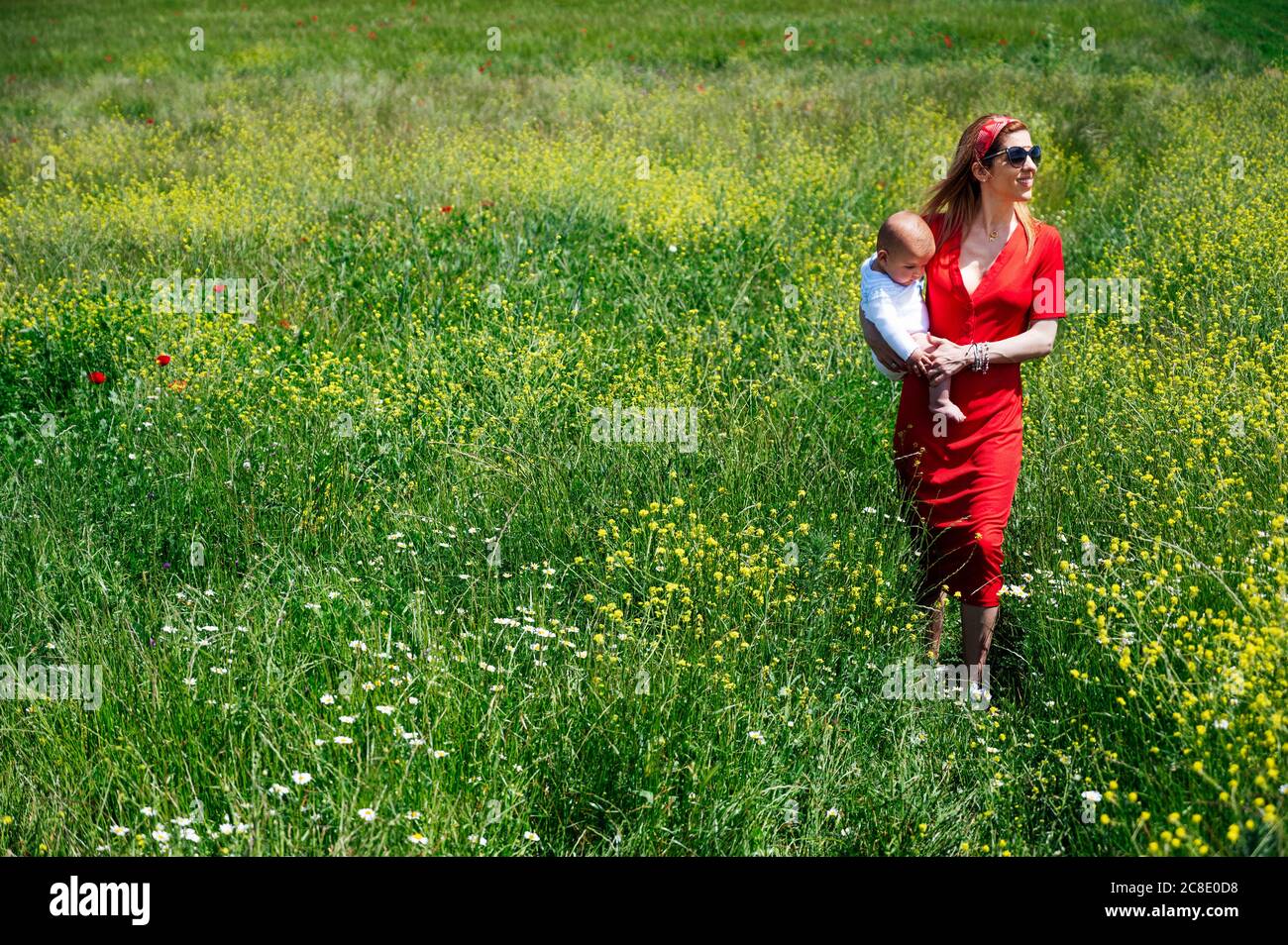 Frau trägt Baby Sohn während des Spazierens auf grasbewachsenen Land während Sonniger Tag Stockfoto