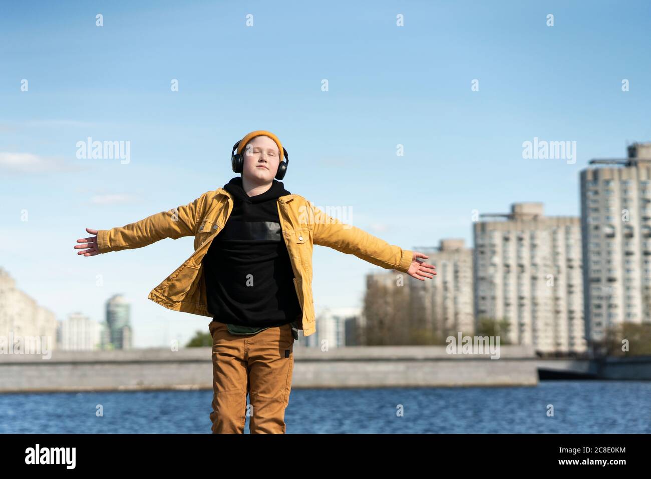 Entspannter Junge, der mit ausgestreckten Armen steht und Musik hört Stadt Stockfoto