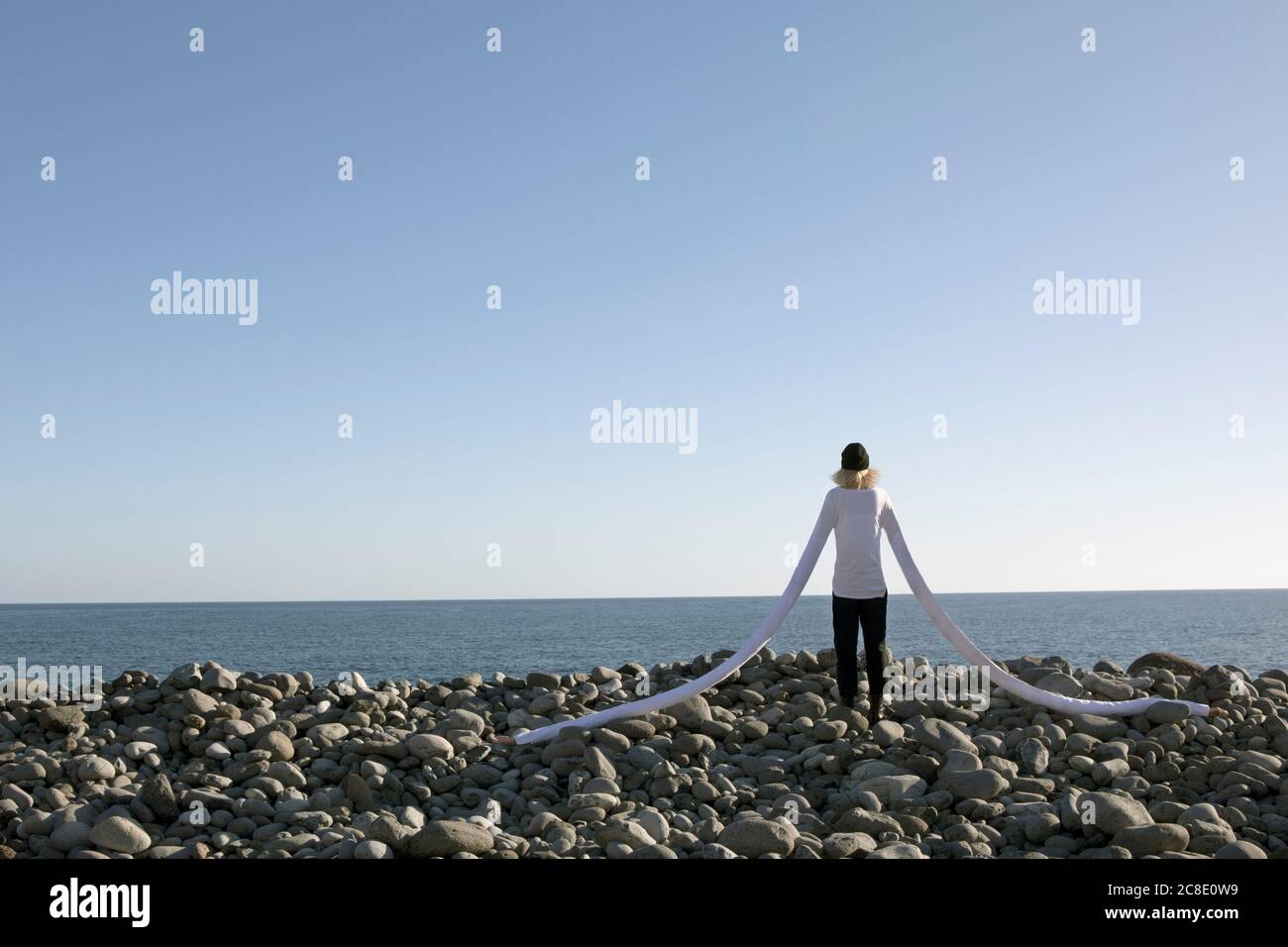 Frau mit künstlichen langen Händen stehen auf Kieselsteinen am Strand Gegen klaren Himmel Stockfoto