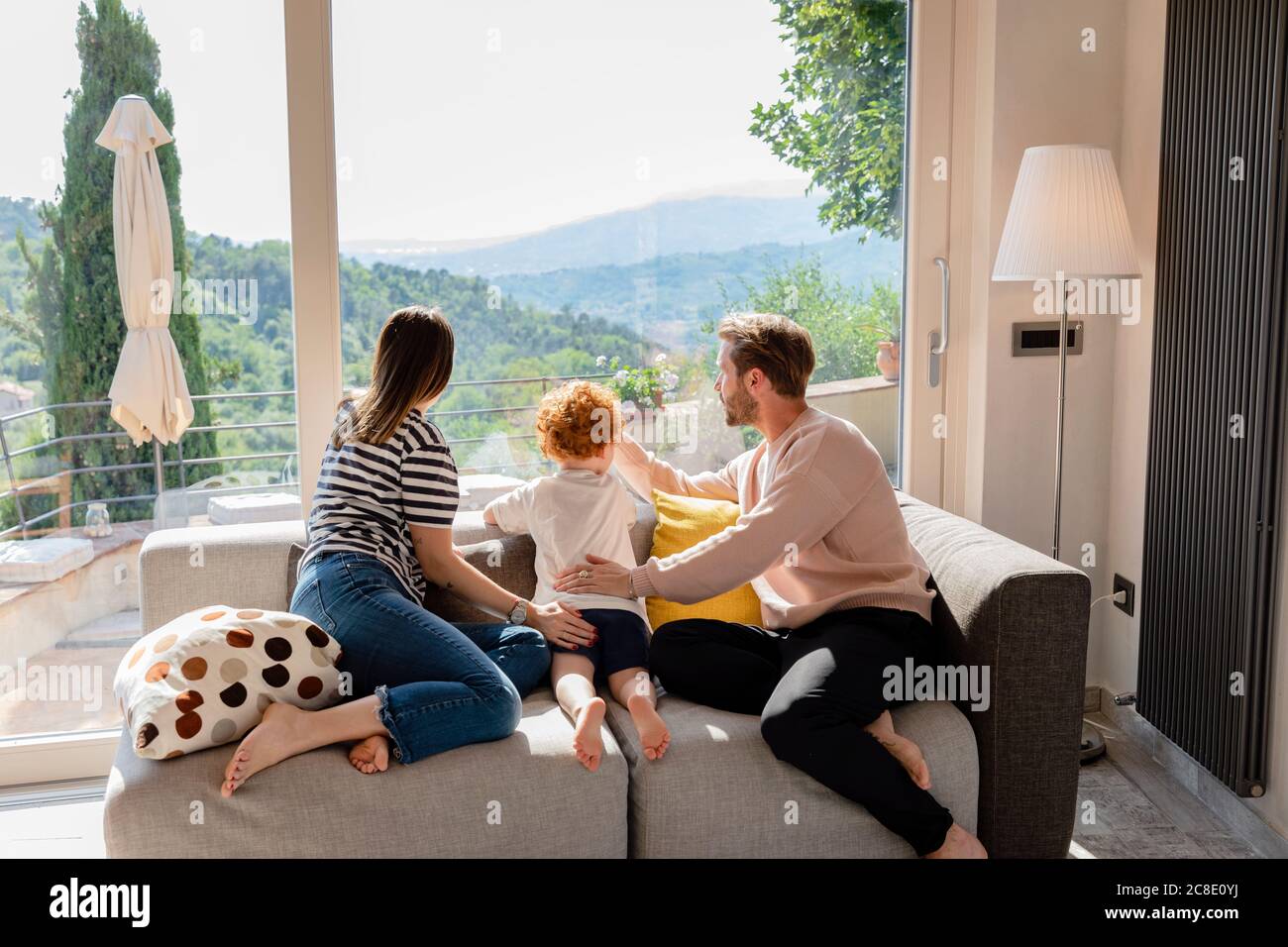 Familie blickt durch das Fenster, während sie auf dem Sofa sitzt Wohnzimmer zu Hause Stockfoto