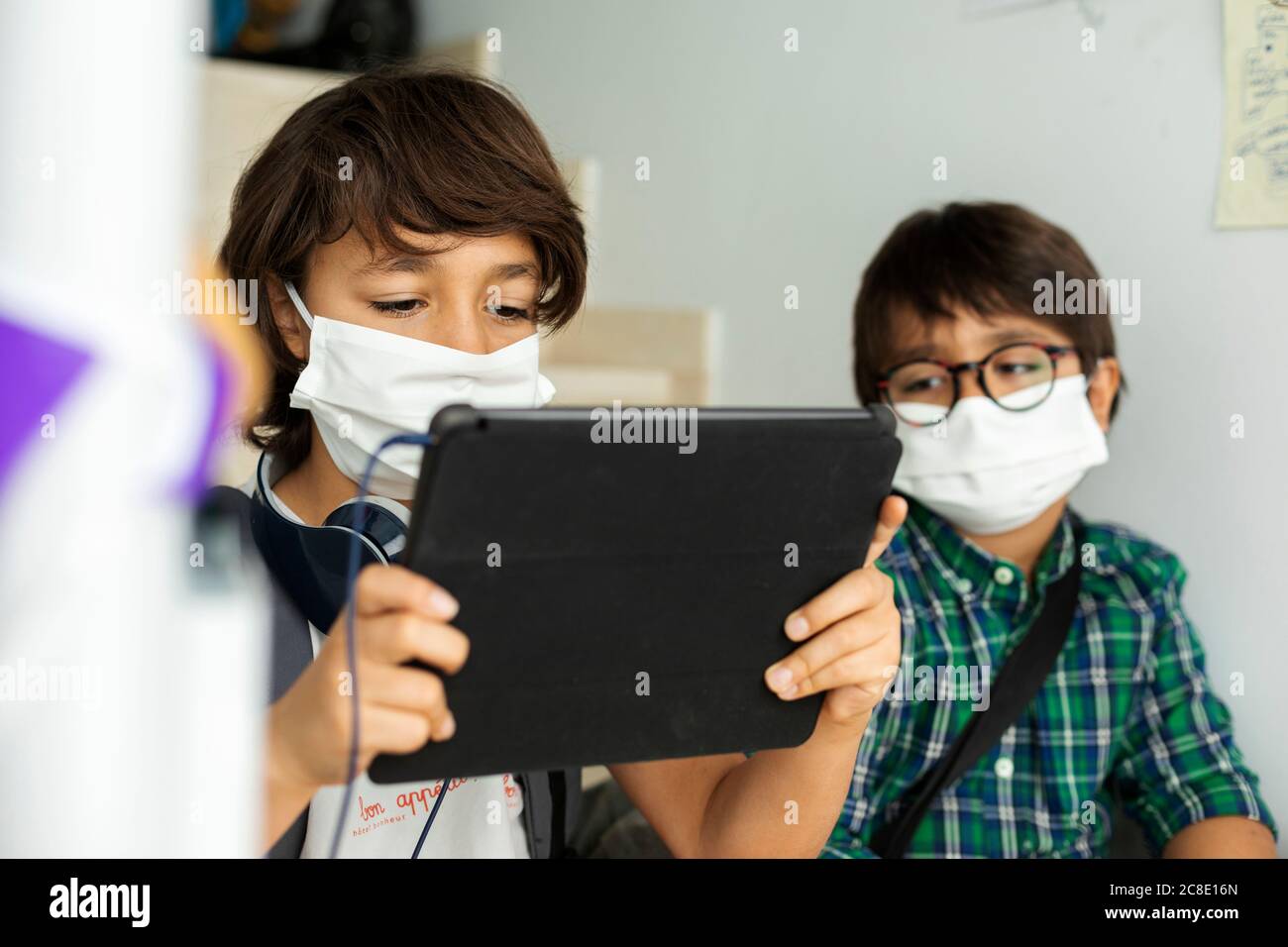 Junge trägt Gesichtsmaske mit digitalen Tablet, während Sie sitzen Distanz mit Freund in der Schule Stockfoto