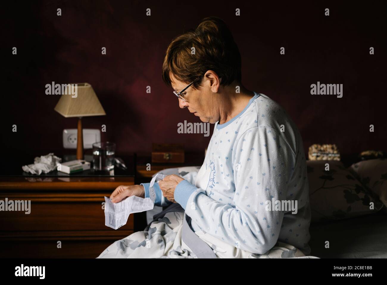 Kranke ältere Frau beim Lesen von verschreibungspflichtigen Medikamenten während des Sitzens Auf dem Bett zu Hause Stockfoto