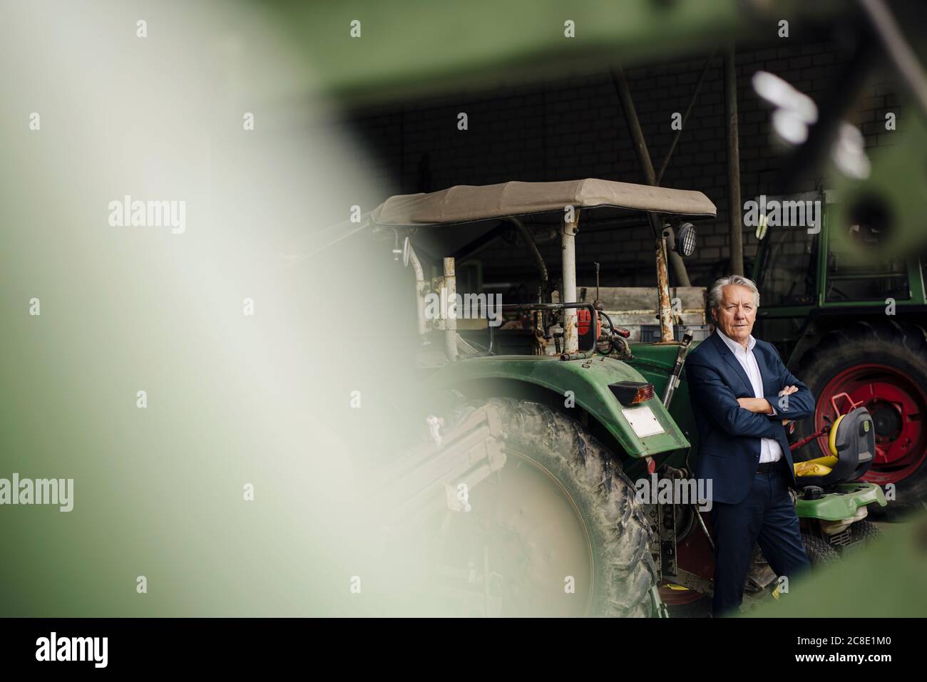 Senior Geschäftsmann auf einem Bauernhof mit Traktor in Scheune Stockfoto