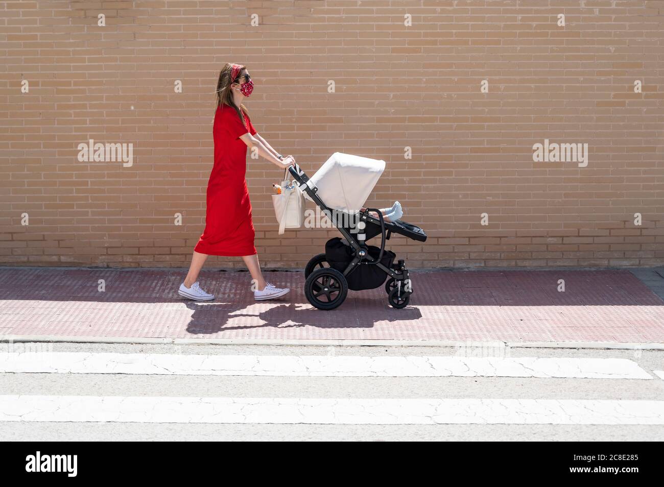 Mutter trägt Maske schieben Sohn in Baby-Wagen beim Gehen Auf dem Bürgersteig Stockfoto