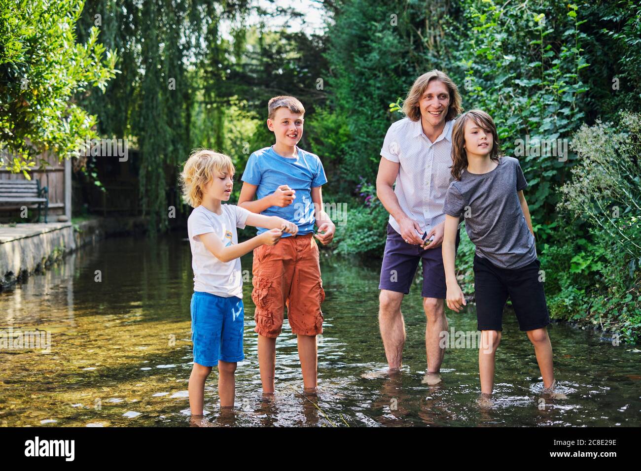 Glücklicher Vater spielt mit Jungen im Bach am Wald Stockfoto